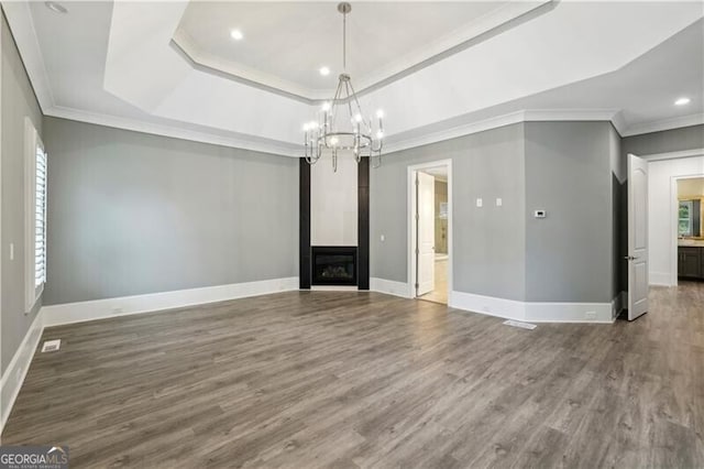 unfurnished dining area featuring wood-type flooring, a tray ceiling, crown molding, and a notable chandelier