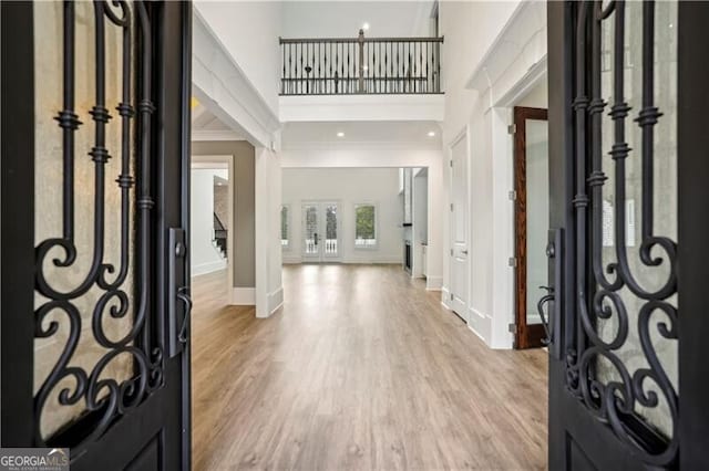 foyer entrance featuring a towering ceiling, ornamental molding, and light hardwood / wood-style flooring