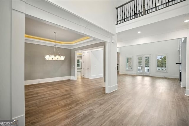 unfurnished living room with a chandelier, a towering ceiling, hardwood / wood-style flooring, and a raised ceiling