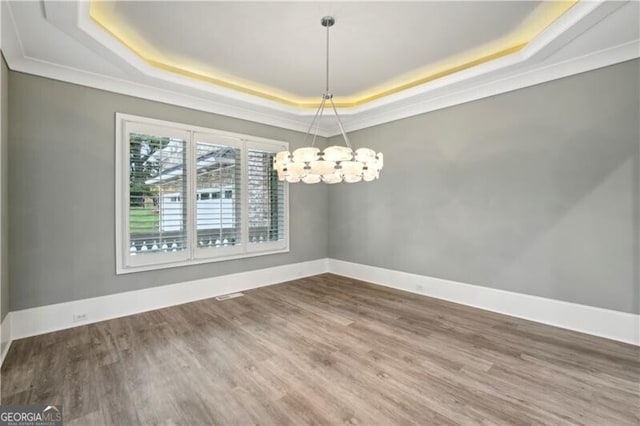 unfurnished dining area with ornamental molding, wood-type flooring, a tray ceiling, and an inviting chandelier