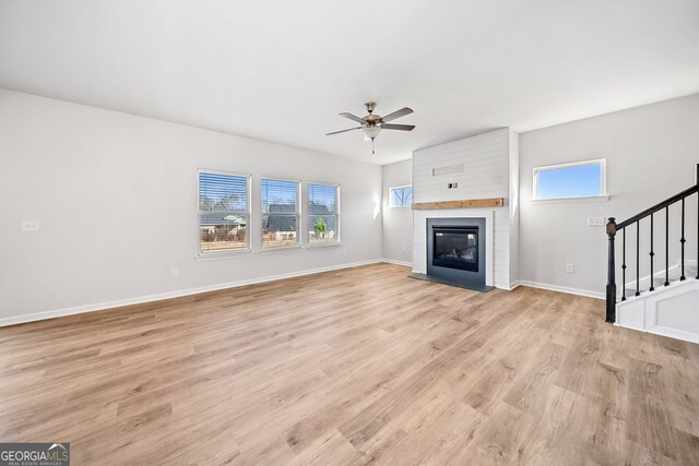 unfurnished living room with plenty of natural light, a large fireplace, ceiling fan, and light hardwood / wood-style flooring