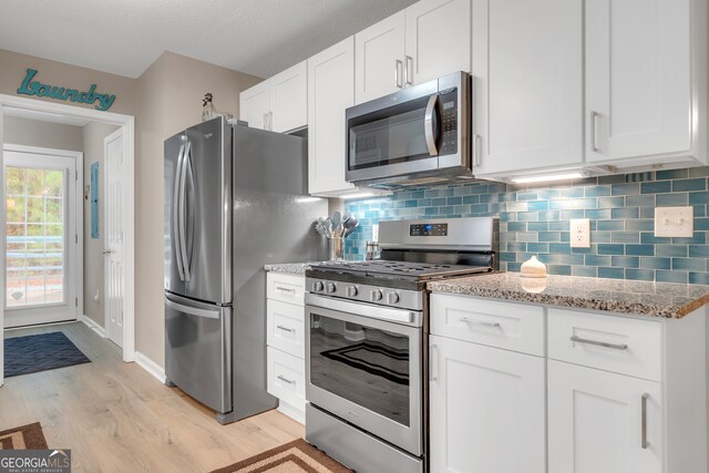 kitchen featuring white cabinets, light stone countertops, light wood-type flooring, and appliances with stainless steel finishes