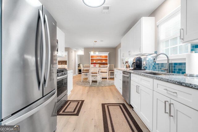 kitchen with sink, hanging light fixtures, appliances with stainless steel finishes, white cabinets, and light wood-type flooring