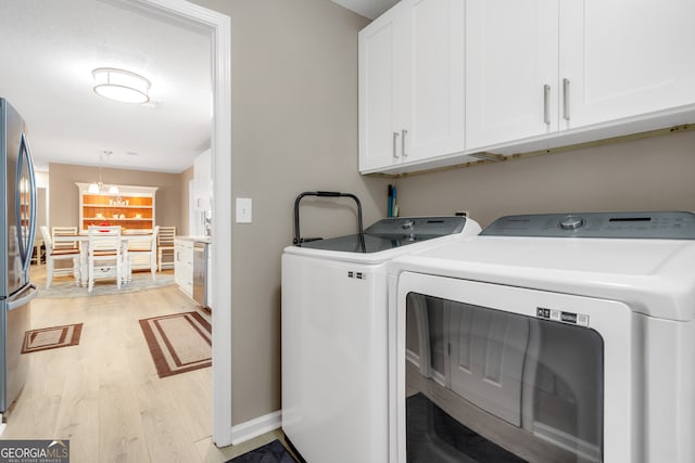 clothes washing area featuring washer and clothes dryer, a notable chandelier, cabinets, and light wood-type flooring