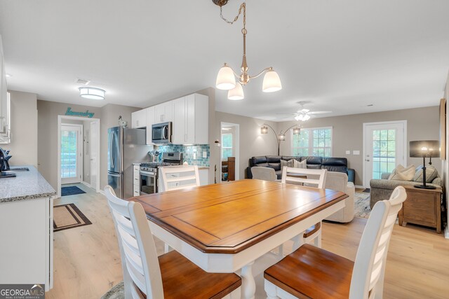 dining space featuring sink, ceiling fan with notable chandelier, and light wood-type flooring