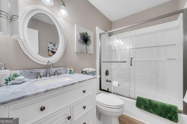 full bathroom with combined bath / shower with glass door, vanity, hardwood / wood-style flooring, and toilet