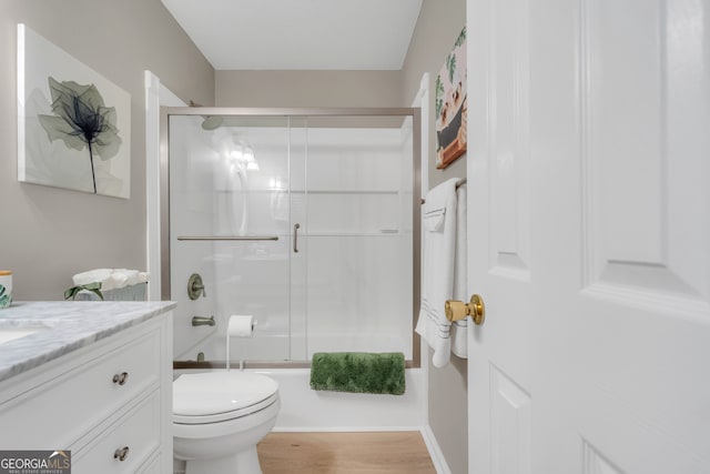 full bathroom with bath / shower combo with glass door, vanity, wood-type flooring, and toilet