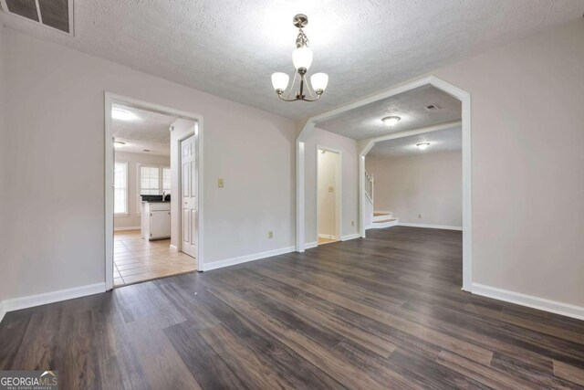 unfurnished dining area featuring a textured ceiling, dark hardwood / wood-style floors, and an inviting chandelier