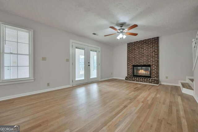 unfurnished living room featuring light hardwood / wood-style floors, ceiling fan, a textured ceiling, a fireplace, and french doors