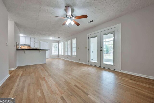 unfurnished living room featuring french doors, light wood-type flooring, a textured ceiling, and ceiling fan