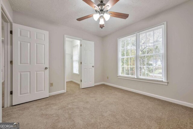 unfurnished bedroom with a spacious closet, light carpet, and ceiling fan