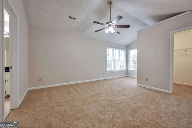 unfurnished bedroom featuring a spacious closet, ceiling fan, light carpet, and vaulted ceiling