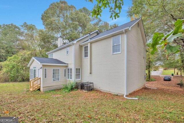 rear view of house with central AC and a yard