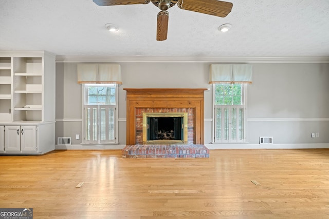 unfurnished living room with light hardwood / wood-style floors, ceiling fan, a textured ceiling, crown molding, and a brick fireplace