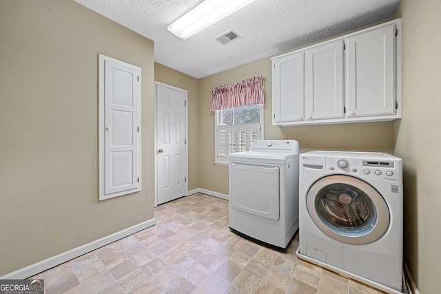 washroom with a textured ceiling, washer and clothes dryer, and cabinets