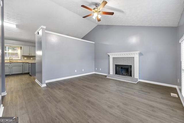 unfurnished living room featuring dark hardwood / wood-style flooring, a brick fireplace, vaulted ceiling, ceiling fan, and sink