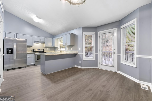 kitchen with kitchen peninsula, appliances with stainless steel finishes, light stone counters, vaulted ceiling, and wood-type flooring