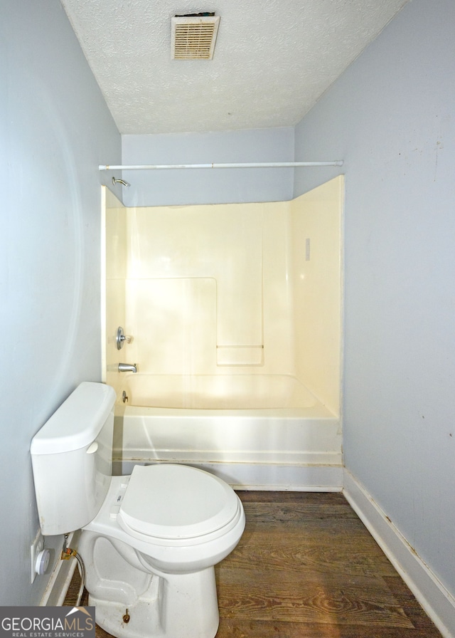 bathroom with shower / bathing tub combination, wood-type flooring, a textured ceiling, and toilet