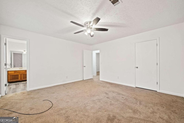 unfurnished bedroom featuring ensuite bathroom, carpet flooring, a textured ceiling, and ceiling fan