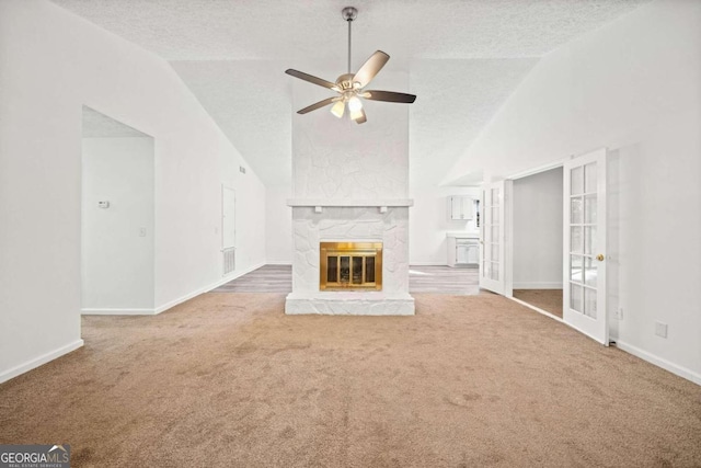 unfurnished living room with ceiling fan, a stone fireplace, a textured ceiling, and carpet