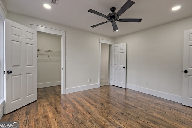 unfurnished bedroom with dark wood-type flooring, ceiling fan, a walk in closet, and a closet