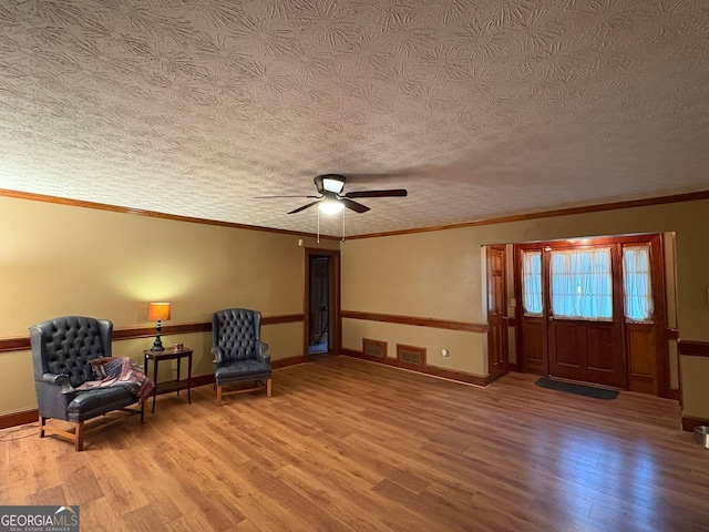 living area featuring a textured ceiling, light wood-type flooring, ceiling fan, and crown molding