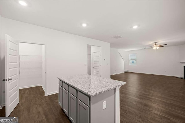 kitchen featuring gray cabinetry, light stone counters, dark hardwood / wood-style flooring, a kitchen island, and ceiling fan