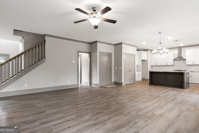 unfurnished living room featuring ceiling fan with notable chandelier, wood-type flooring, and crown molding