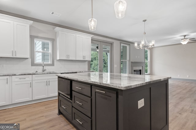 kitchen featuring stainless steel microwave, white cabinets, decorative light fixtures, and ceiling fan with notable chandelier