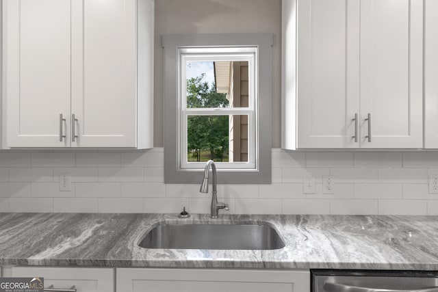 kitchen with white cabinets, backsplash, light stone countertops, and sink