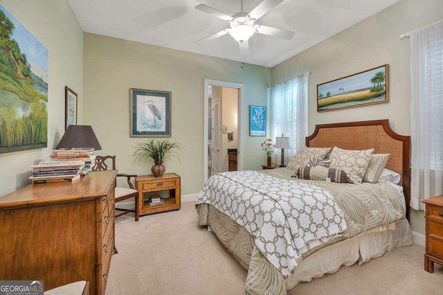 bedroom featuring ceiling fan, light colored carpet, and ensuite bath