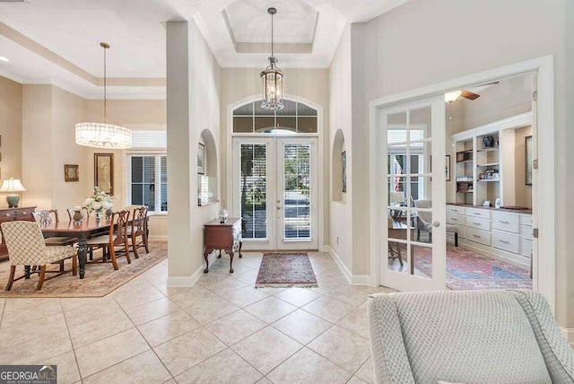 tiled entryway featuring a towering ceiling, a notable chandelier, a tray ceiling, ornamental molding, and french doors