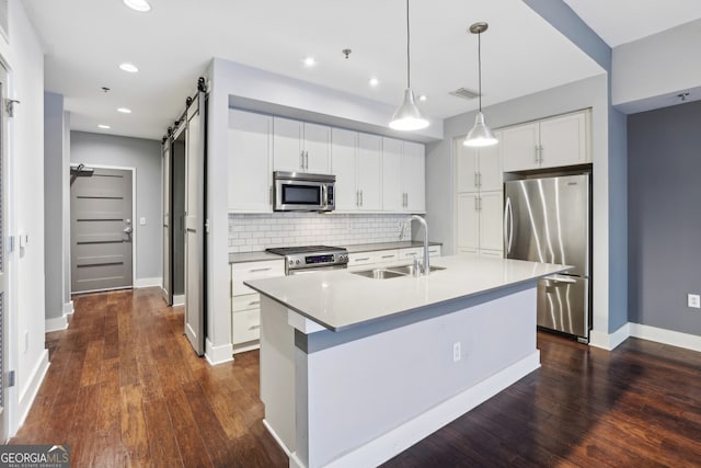 kitchen featuring appliances with stainless steel finishes, dark hardwood / wood-style floors, white cabinets, a kitchen island with sink, and a barn door