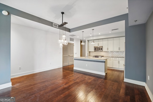 kitchen with white cabinets, a kitchen island with sink, decorative light fixtures, and dark wood-type flooring