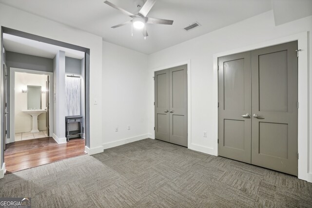 unfurnished bedroom with multiple closets, light hardwood / wood-style floors, ceiling fan, and ensuite bath