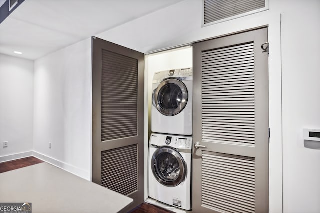 laundry area featuring stacked washer and dryer and dark hardwood / wood-style flooring