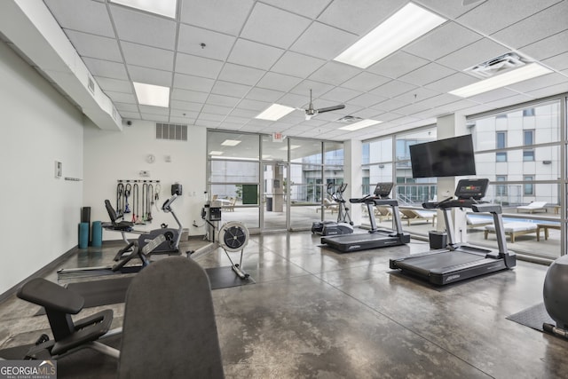 workout area with ceiling fan, a wall of windows, a paneled ceiling, and concrete floors