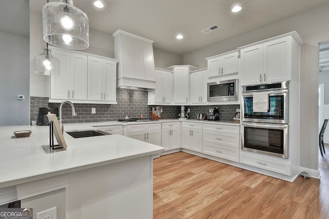 kitchen featuring pendant lighting, sink, custom range hood, appliances with stainless steel finishes, and white cabinetry