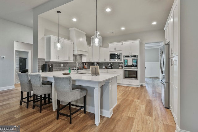 kitchen featuring hanging light fixtures, white cabinetry, light hardwood / wood-style floors, kitchen peninsula, and stainless steel appliances