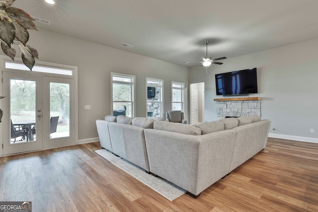 living room with ceiling fan, a stone fireplace, and light wood-type flooring