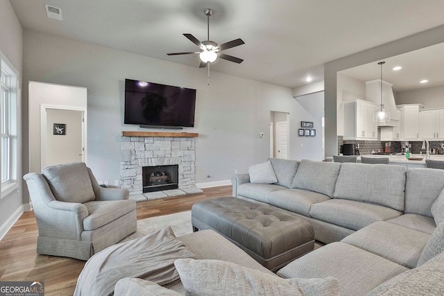 living room with light hardwood / wood-style floors, a stone fireplace, and ceiling fan