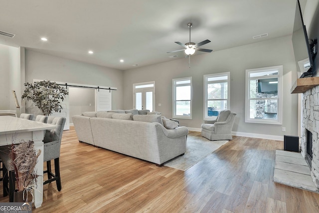 living room featuring ceiling fan, a barn door, light hardwood / wood-style floors, and a fireplace