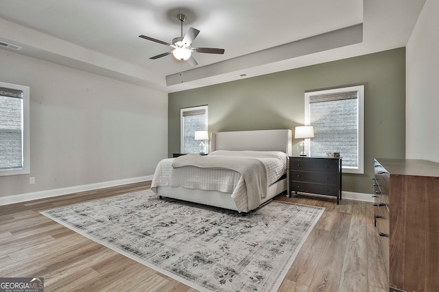 bedroom featuring ceiling fan, light hardwood / wood-style floors, and a tray ceiling