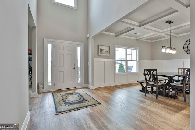 foyer with beam ceiling, coffered ceiling, an inviting chandelier, light hardwood / wood-style flooring, and ornamental molding