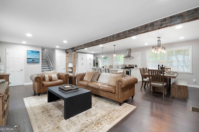 living room with dark wood-type flooring, beamed ceiling, a wealth of natural light, and a chandelier