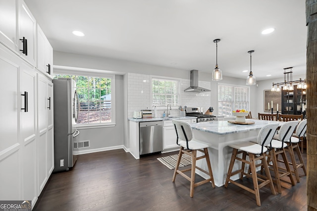 kitchen with stainless steel appliances, wall chimney range hood, dark hardwood / wood-style flooring, pendant lighting, and white cabinets