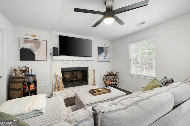 living room featuring a stone fireplace and ceiling fan