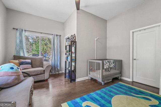 bedroom with a crib, dark hardwood / wood-style floors, and vaulted ceiling