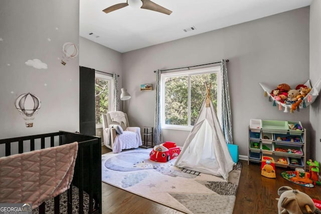 bedroom featuring a crib, ceiling fan, and dark hardwood / wood-style floors