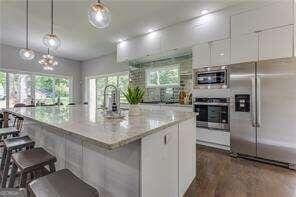 kitchen featuring light stone counters, a center island with sink, stainless steel appliances, decorative light fixtures, and white cabinets